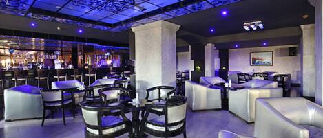 Un área de estar moderna con bar, diferentes disposiciones de asientos y un techo con estampado floral.