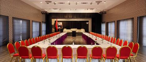 A conference room with a long table, red chairs, and a stage.