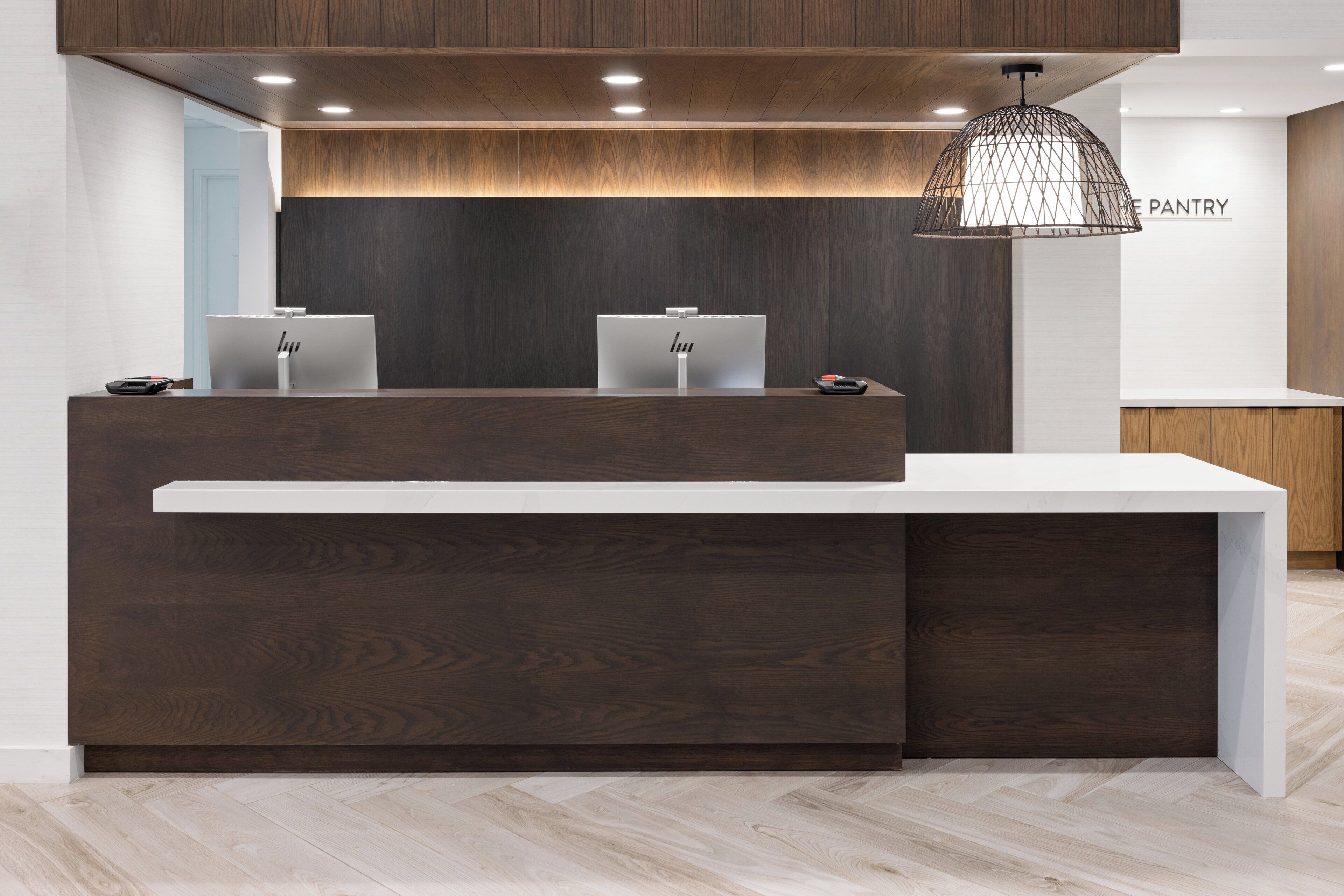 A reception desk with two computer stations, a hanging pendant light, and a sign for the pantry.