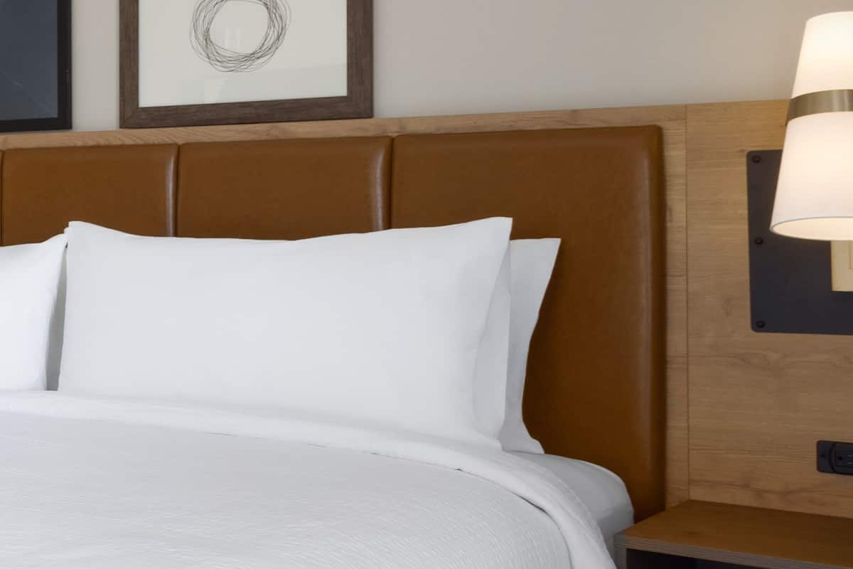 Una cama con cabecera de madera y una mesita de noche con lámpara.