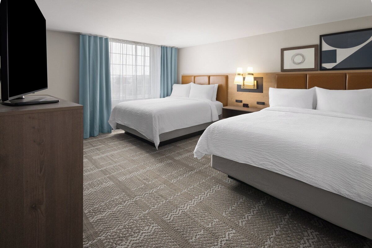 A hotel room with two beds, a TV, a desk, and a window with curtains.