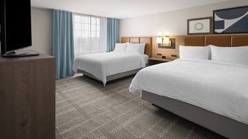 A hotel room with two beds, a TV, a desk, and a window with curtains.