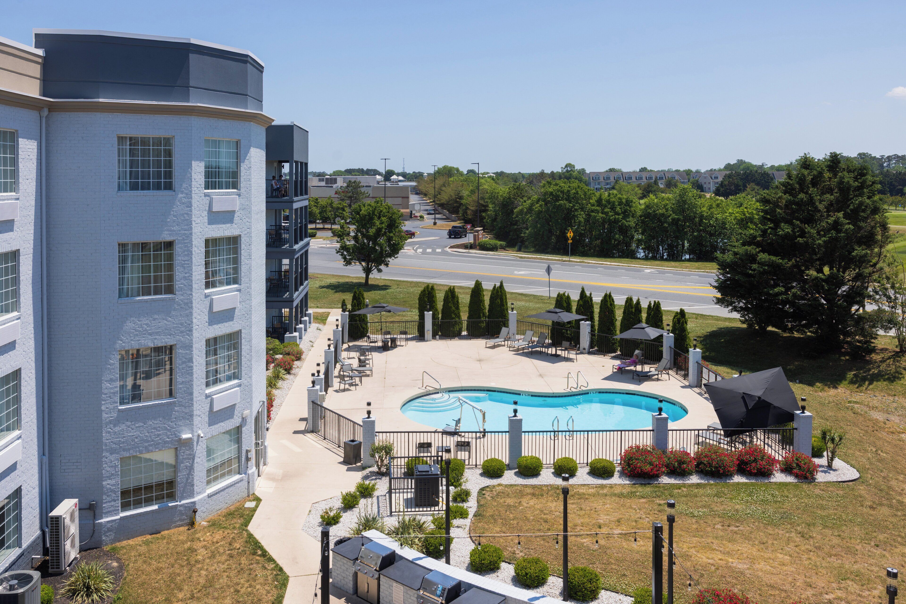A hotel with a swimming pool, outdoor seating, and a view of the road.
