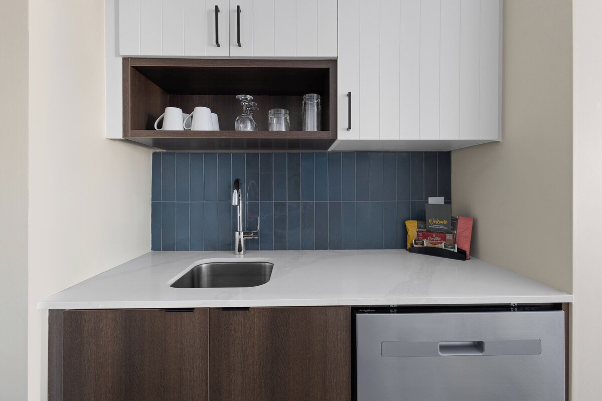A modern kitchen with a built-in dishwasher, a stainless steel sink, and a shelf above the counter holding kitchenware.