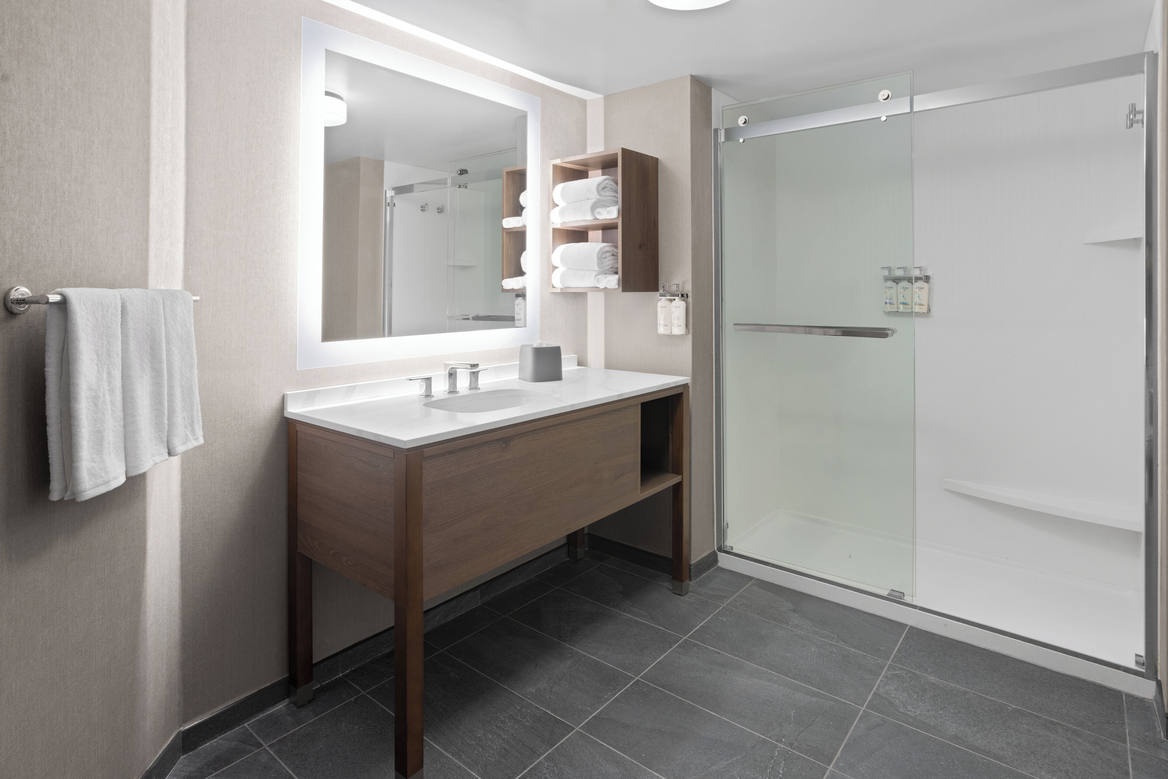 Een moderne badkamer met een grote spiegel, een houten wastafelmeubel, een douchecabine met glazen wanden en een handdoekrek.