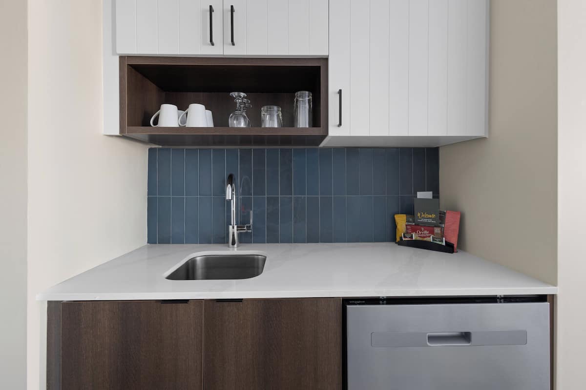 Una cocina moderna con lavavajillas integrado, un lavamanos de acero inoxidable y una repisa sobre la encimera con utensilios de cocina.