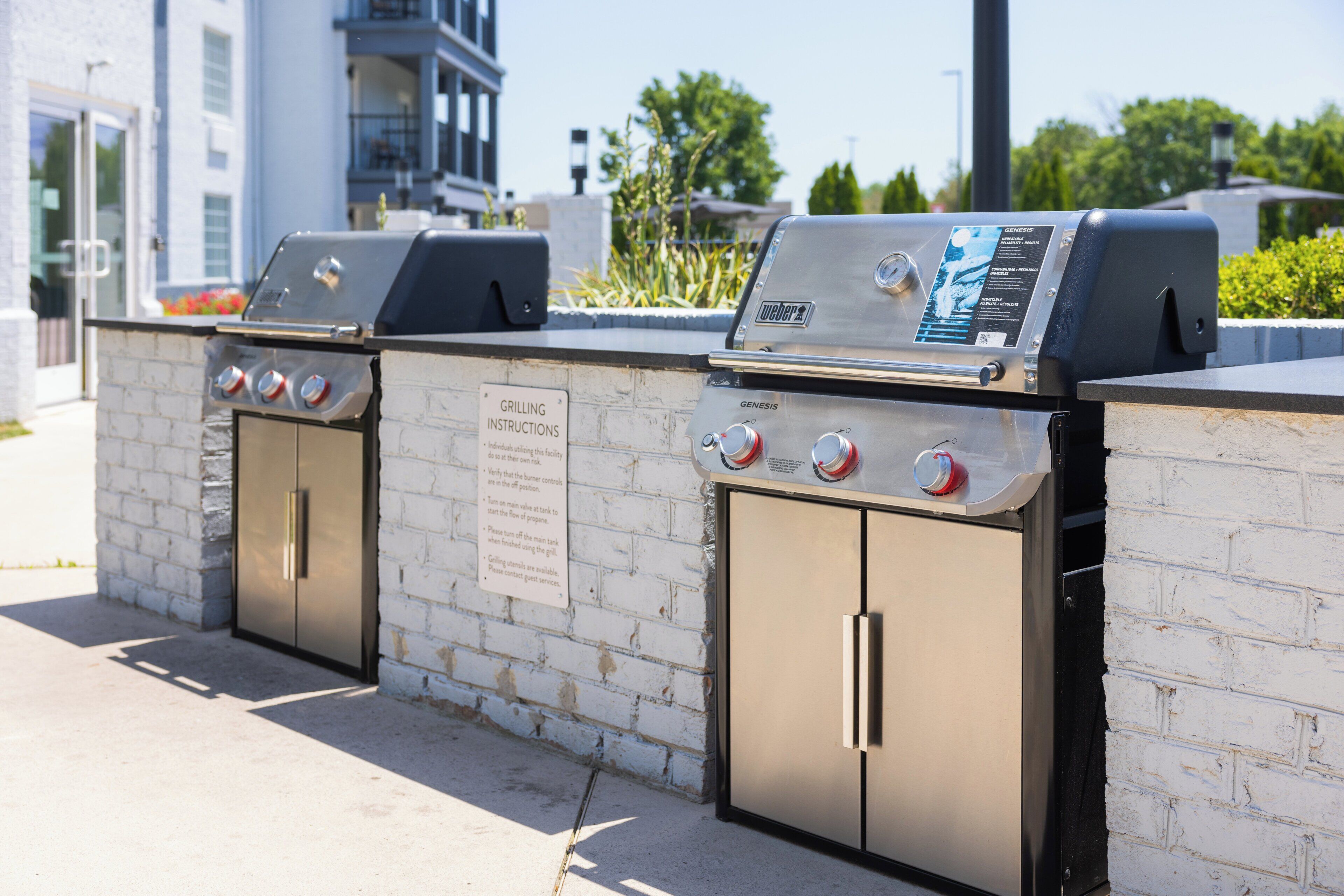 A barbecue grill station with a sign providing grilling instructions, located next to a white brick wall.