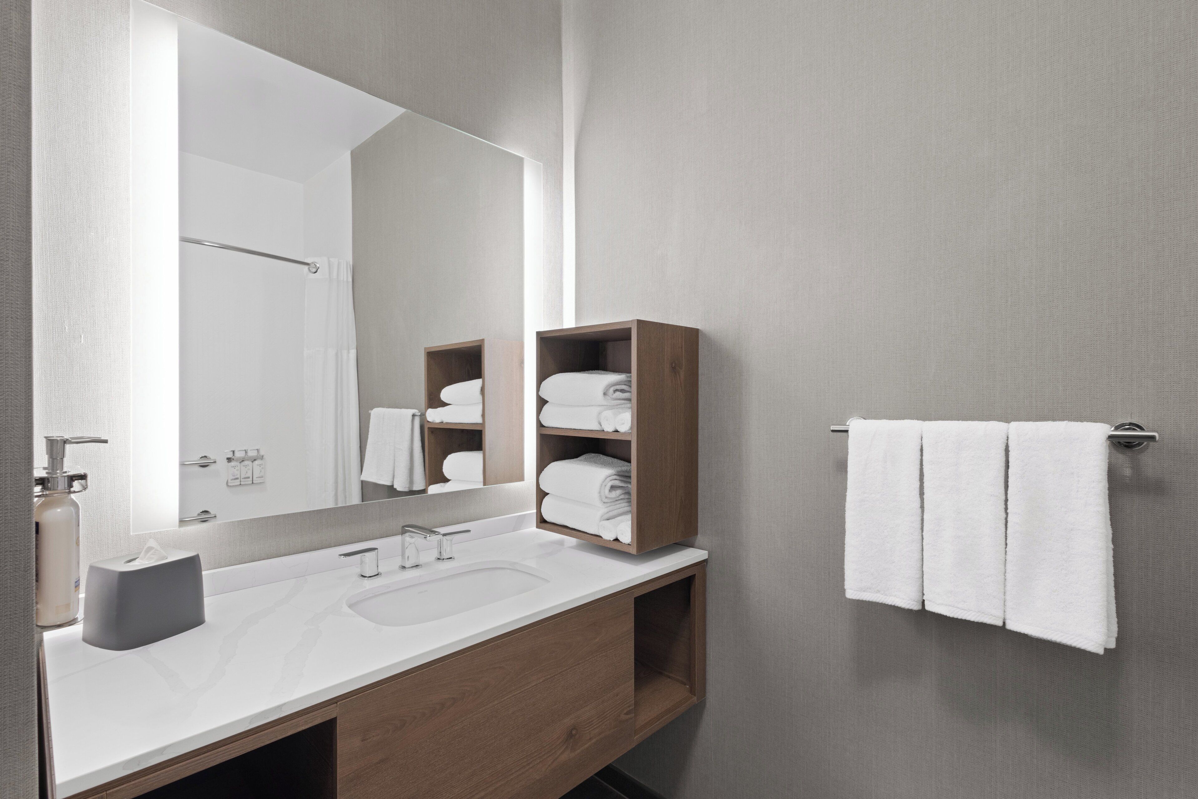 Un baño moderno con tocador de madera, un espejo grande y un perchero para toallas.