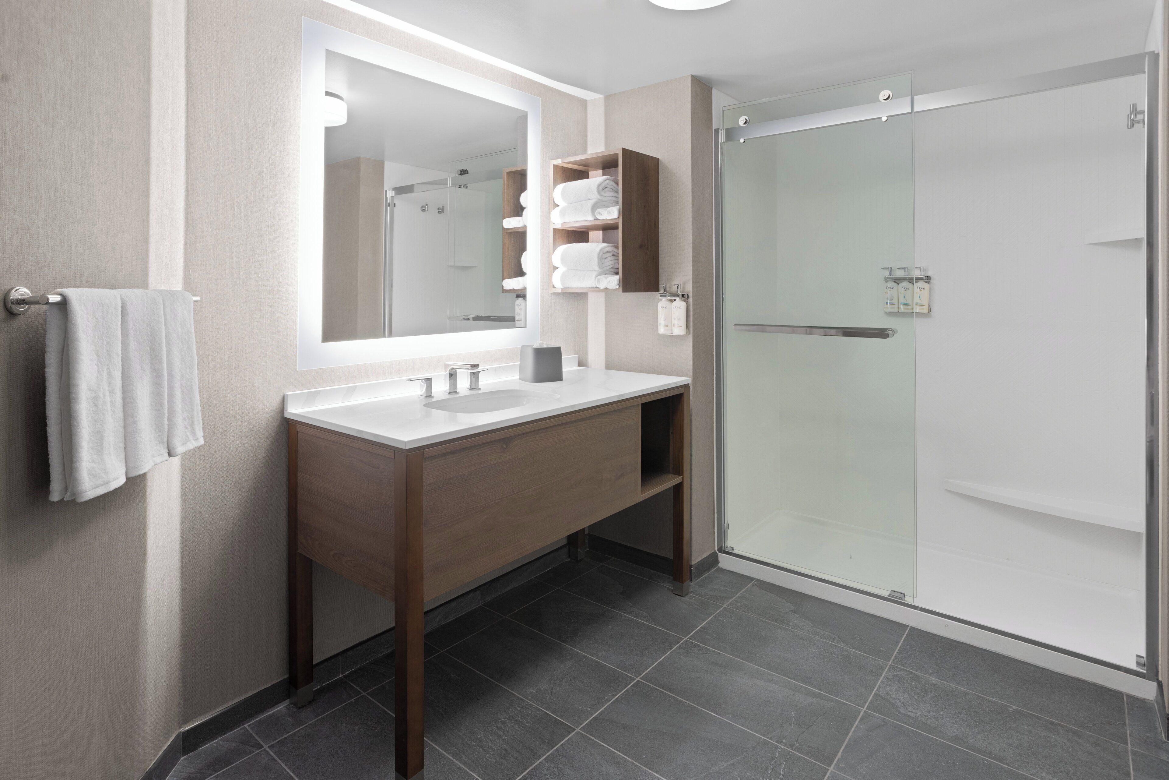 Une salle de bain moderne avec un grand miroir, un meuble-lavabo en bois, une cabine de douche en verre et un porte-serviettes.