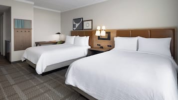 A hotel room with two beds, a desk, a lamp, and a wall-mounted light fixture.
