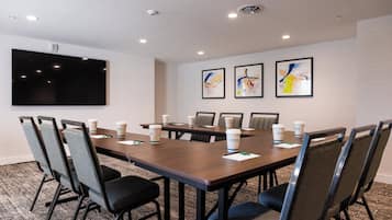 A conference room with a large table, chairs, a flat-screen TV, and abstract art on the wall.