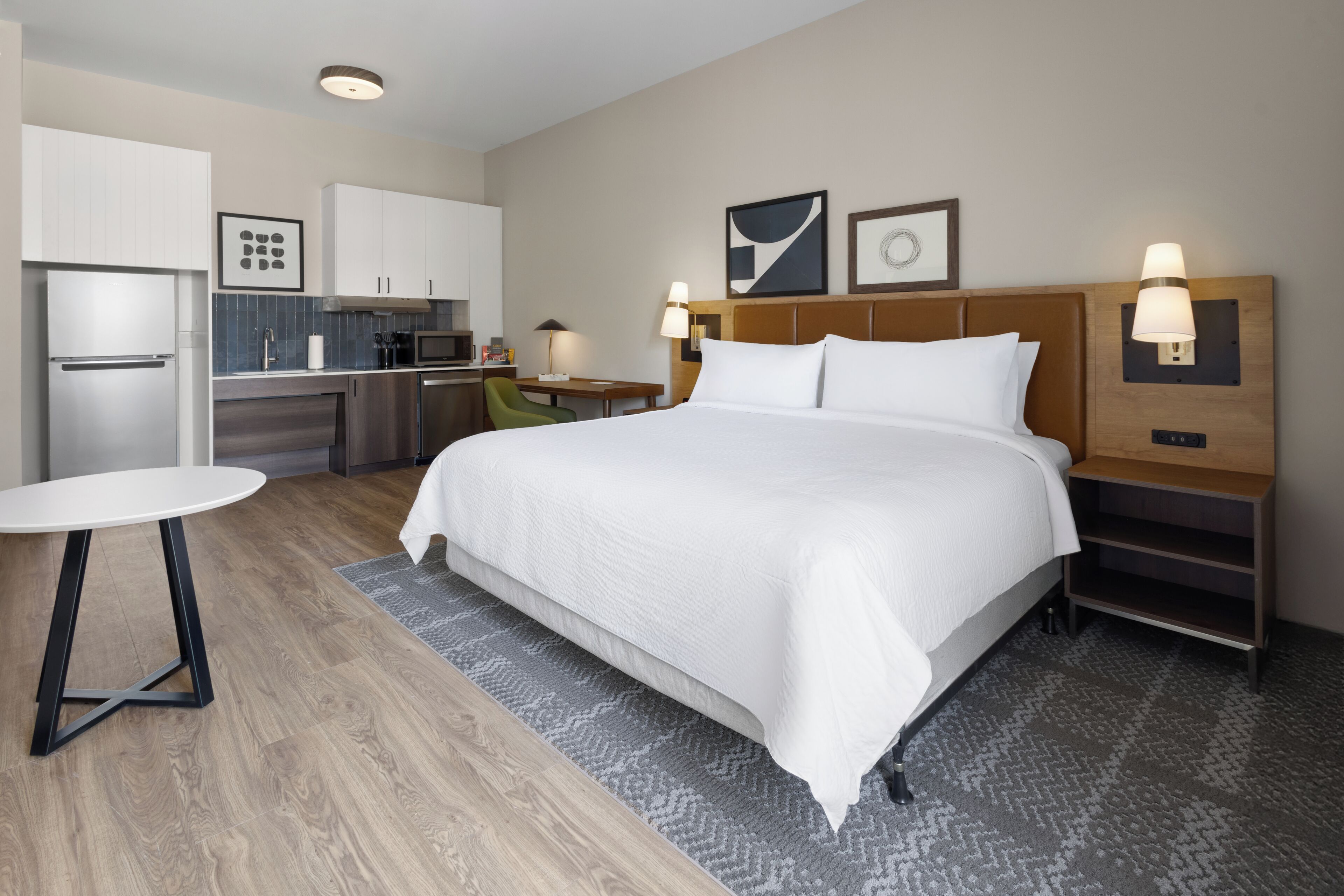 A hotel room with a bed, a desk, a chair, a refrigerator, and a microwave.