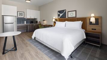 A hotel room with a bed, a desk, a chair, a refrigerator, and a microwave.