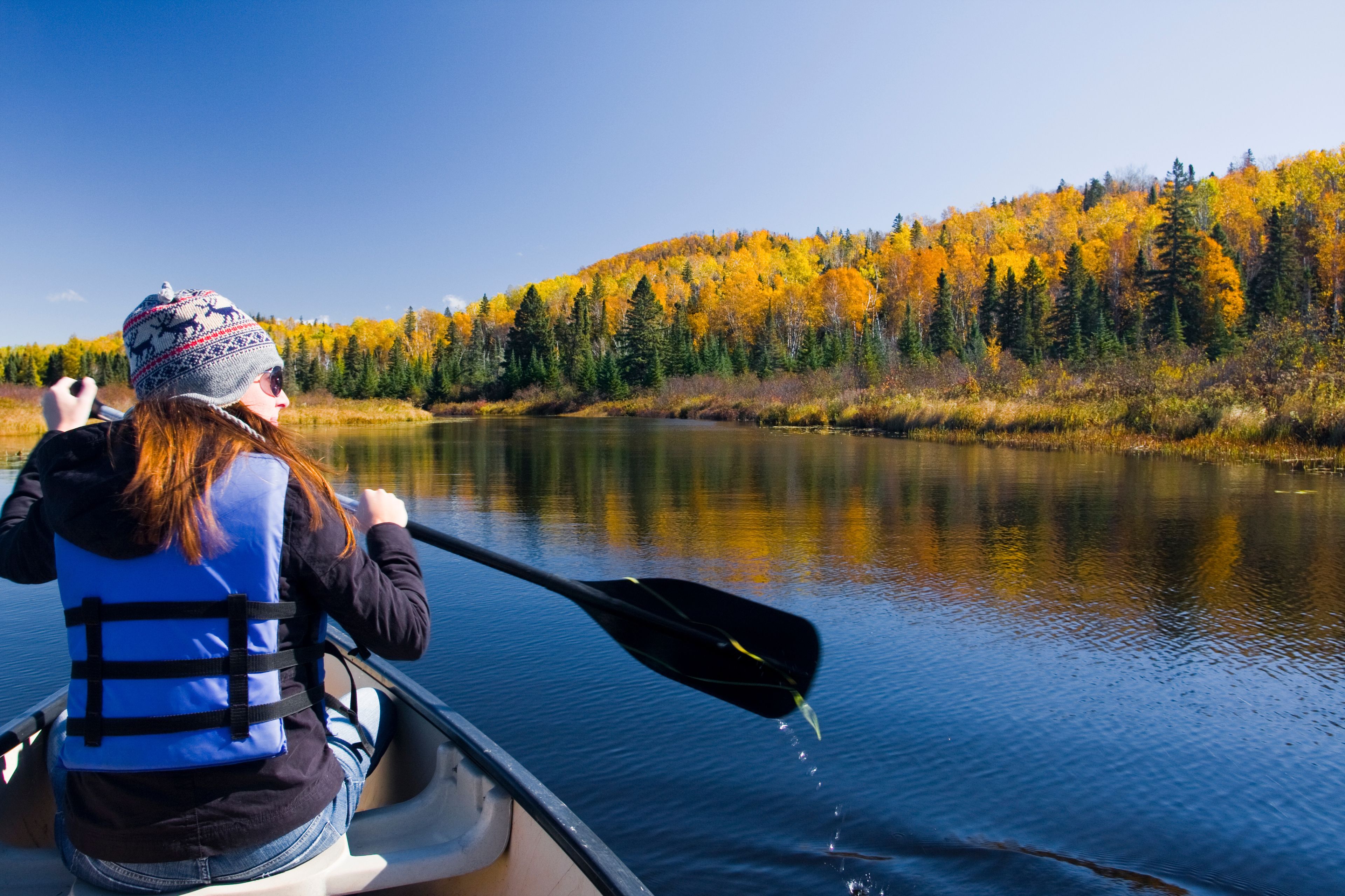 A person in a canoe on a calm river with autumn foliage in the background.