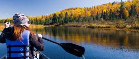 A person in a canoe on a calm river with autumn foliage in the background.