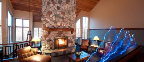 A cozy lounge area with a stone fireplace, leather seating, and a modern light installation.