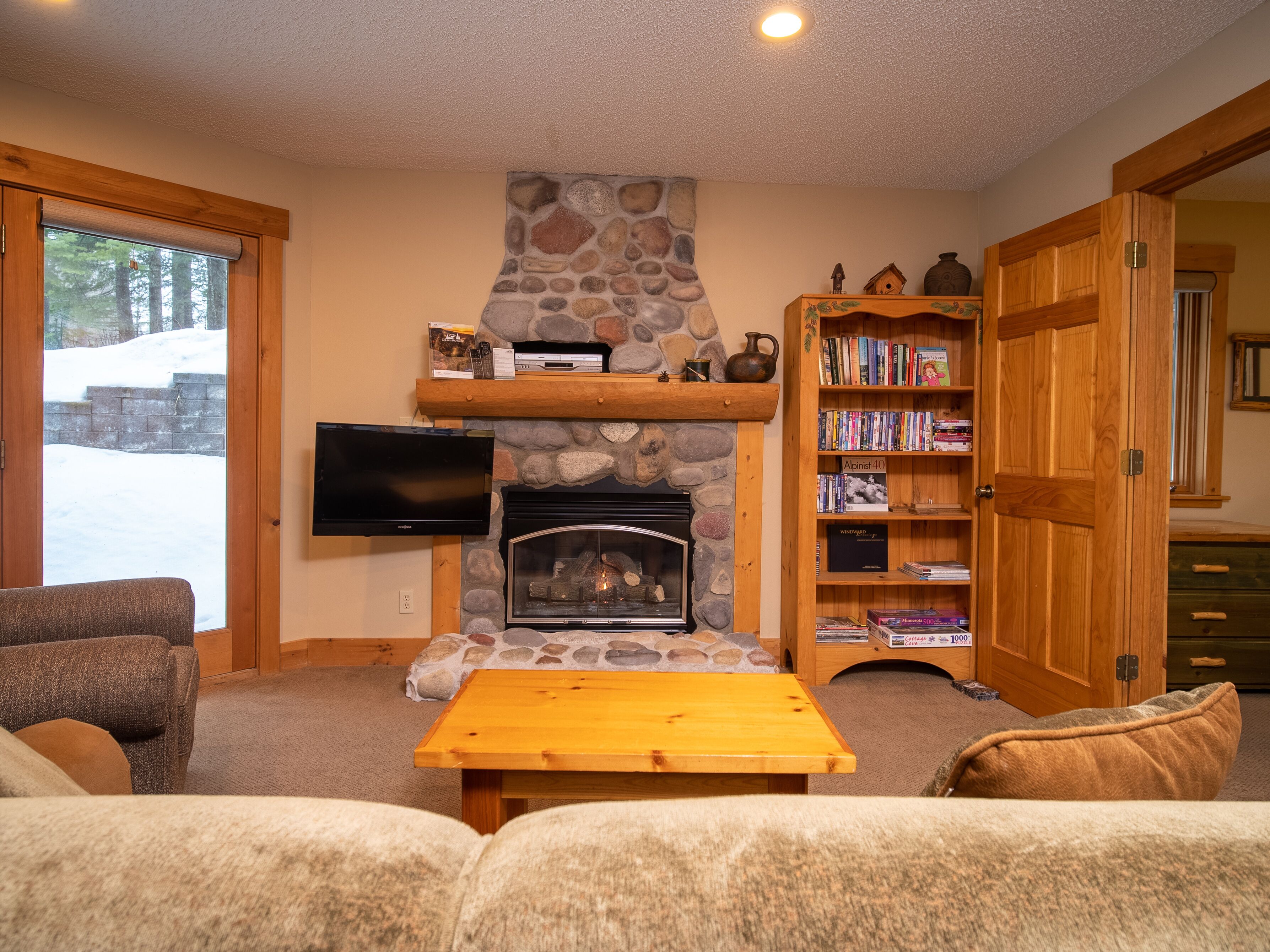 A cozy living room with a stone fireplace, a flat-screen TV, a bookshelf, and a comfortable seating area.