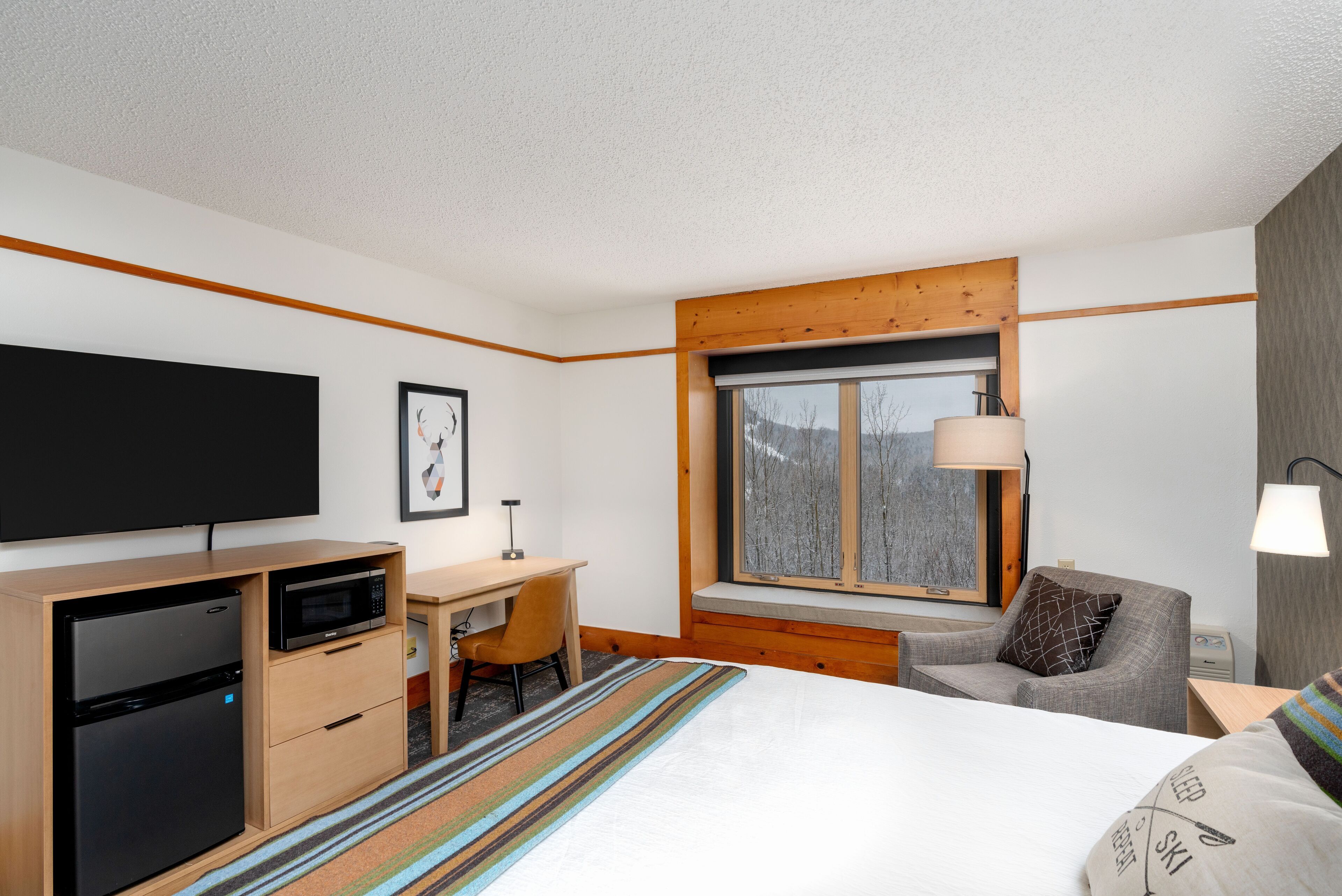 Ein Hotelzimmer mit Bett, Schreibtisch mit Computer, Mikrowelle, Fernseher und Fenster mit Blick auf Bäume.