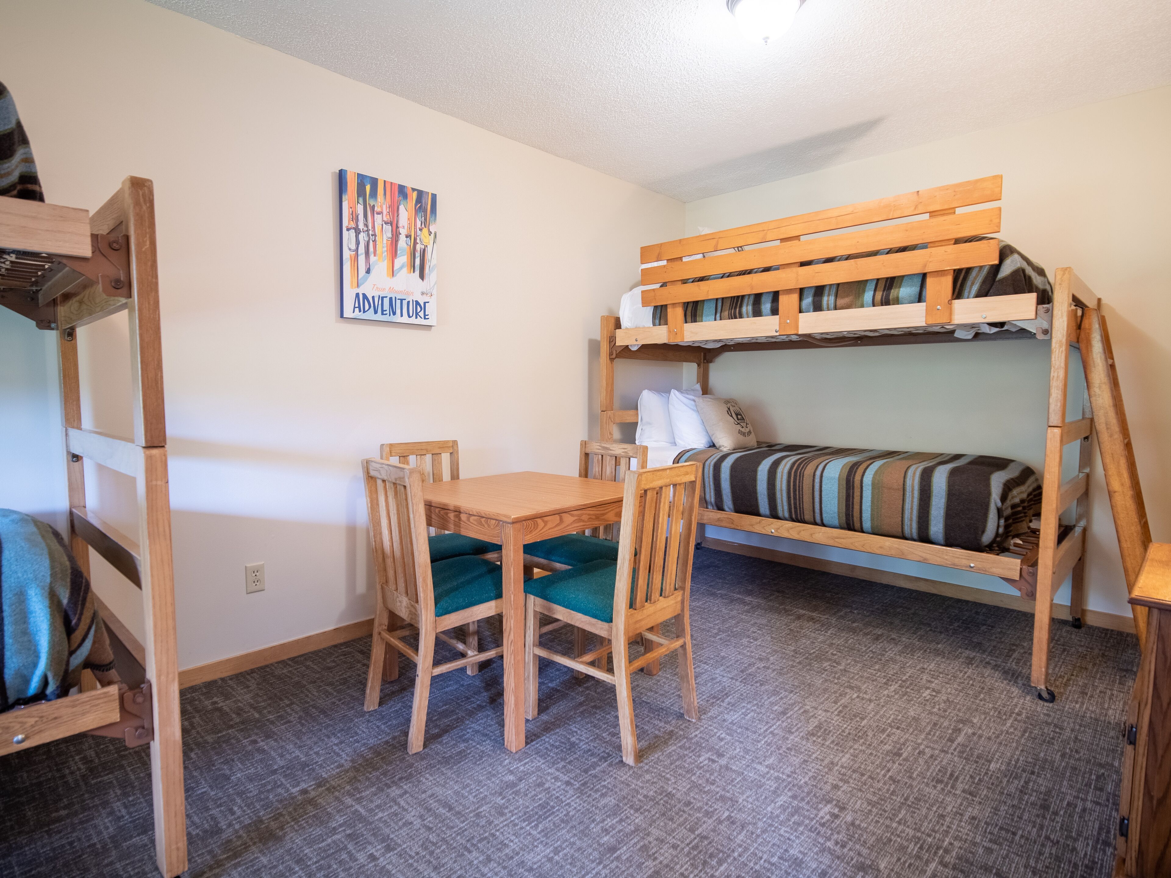 A bunk bed with a striped blanket, a wooden table with two chairs, and a poster on the wall.