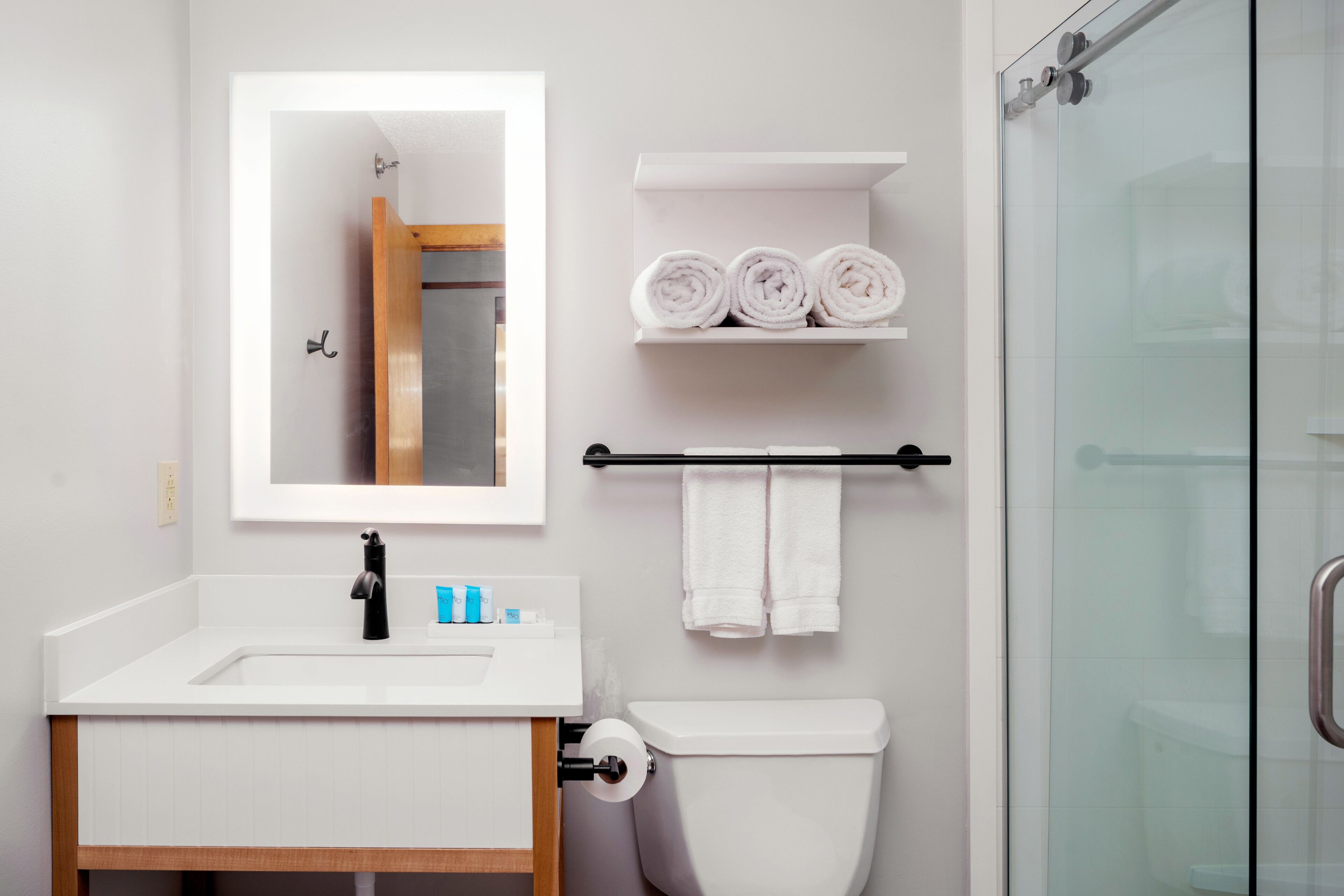 A modern bathroom with a white sink, mirror, and toilet. There are towels and toiletries on the counter.