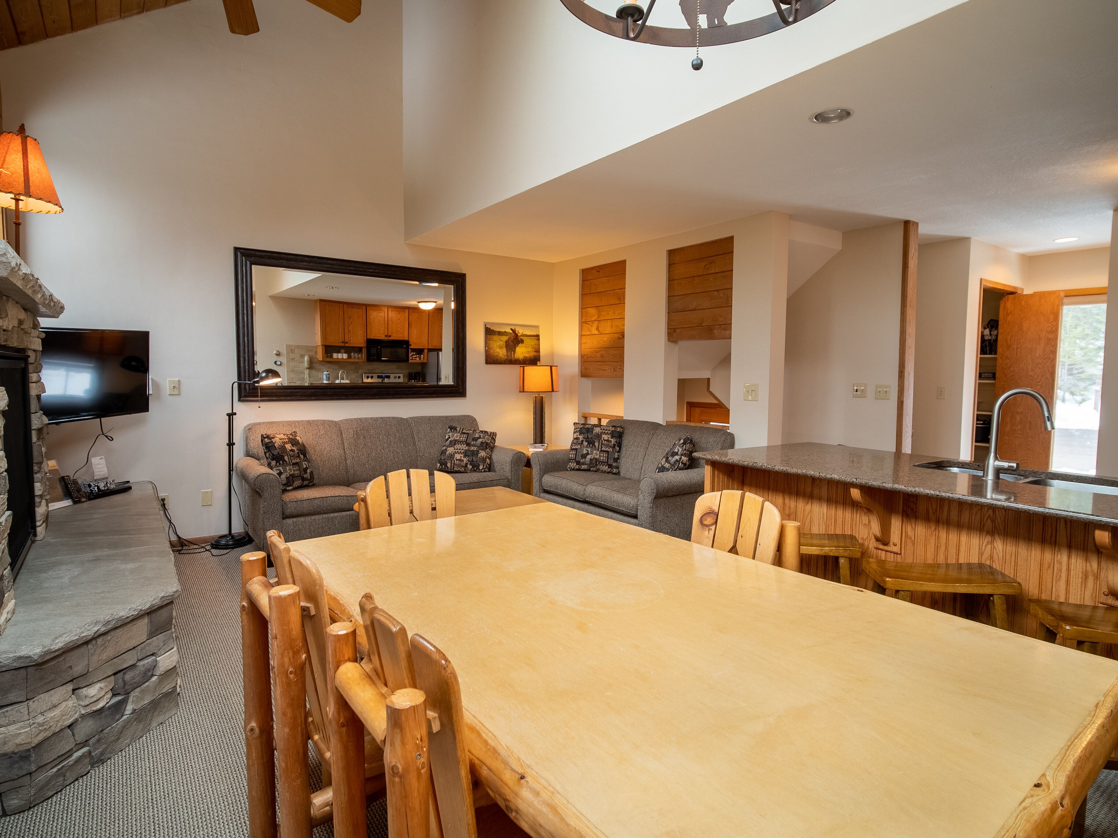 A spacious living area with a large wooden dining table, two sofas, a kitchen area, and a stone fireplace.