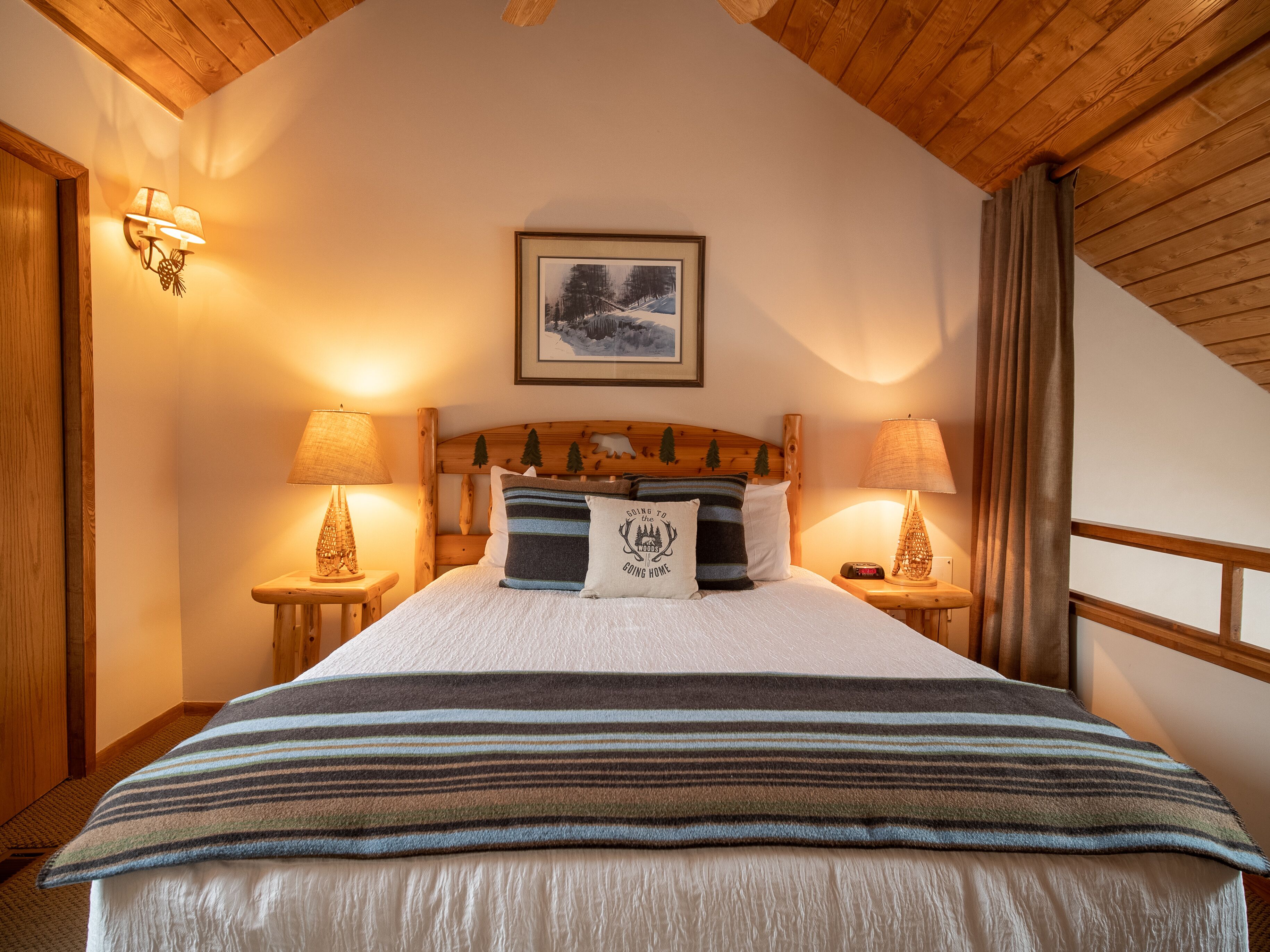 Un dormitorio acogedor con cabecera de madera, cama grande con ropa de cama a rayas, dos lámparas de noche y un cuadro enmarcado en la pared.
