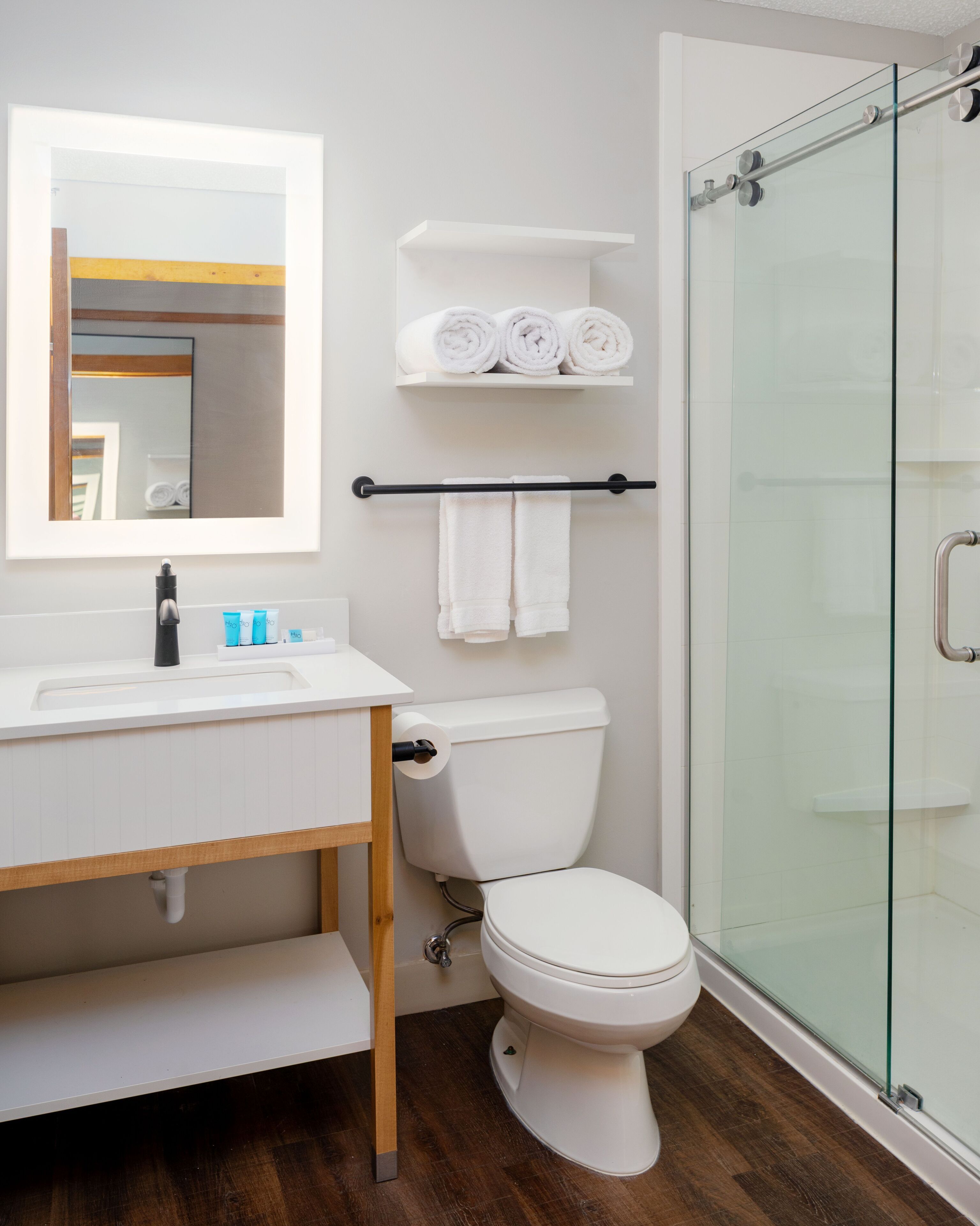 A modern bathroom with a white sink, mirror, and toilet. There is a glass shower enclosure and a towel rack with towels.