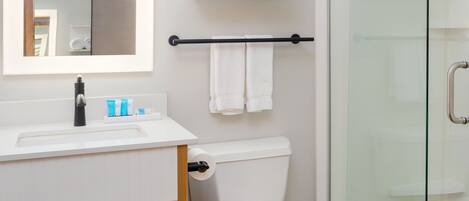 A modern bathroom with a white sink, mirror, and toilet. There is a glass shower enclosure and a towel rack with towels.