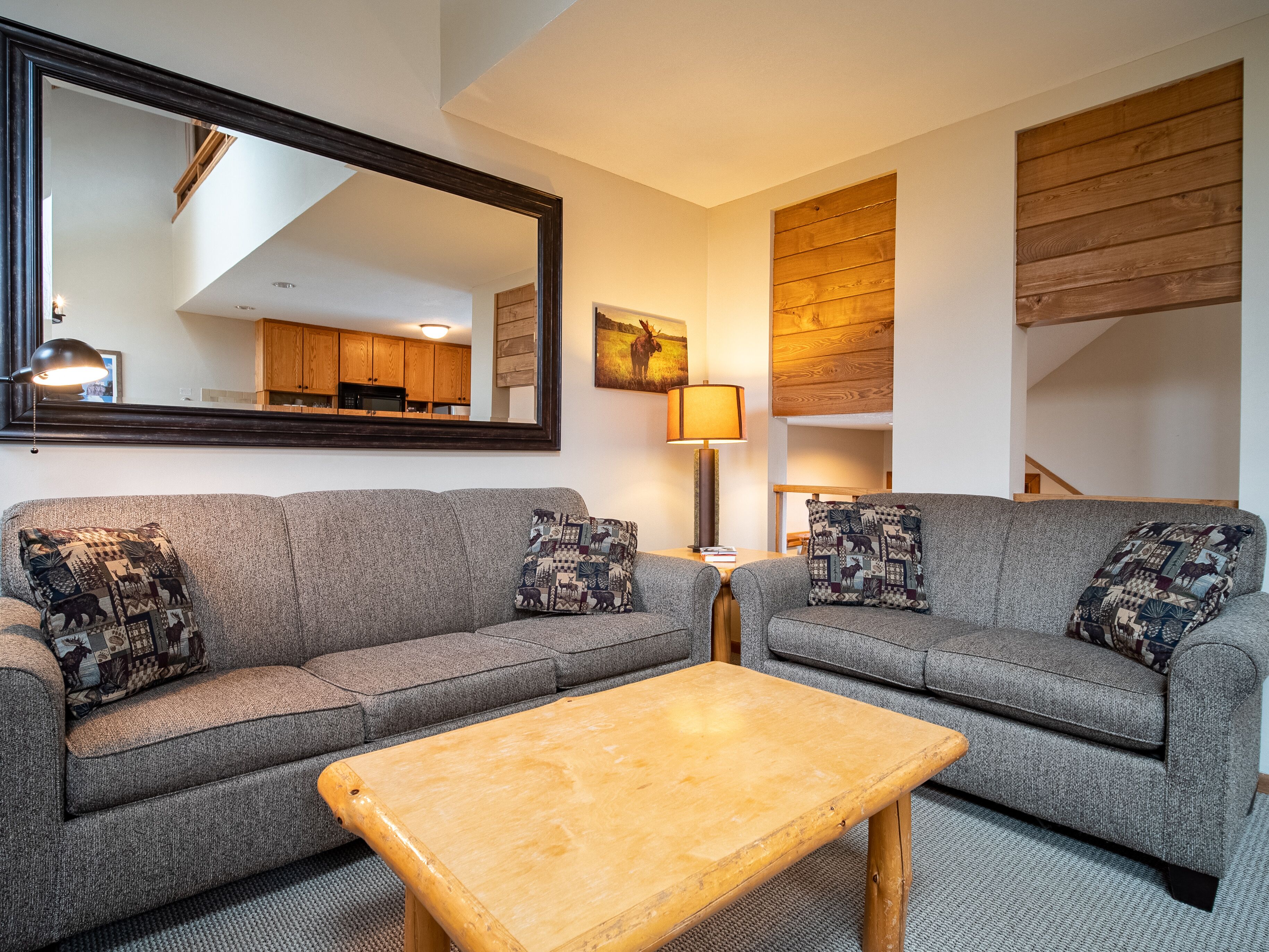 A living room with two grey sofas, a wooden coffee table, a mirror, and a lamp.