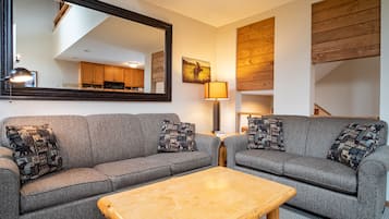 Ein Wohnzimmer mit zwei grauen Sofas, einem Holztisch, einem Spiegel und einer Lampe.