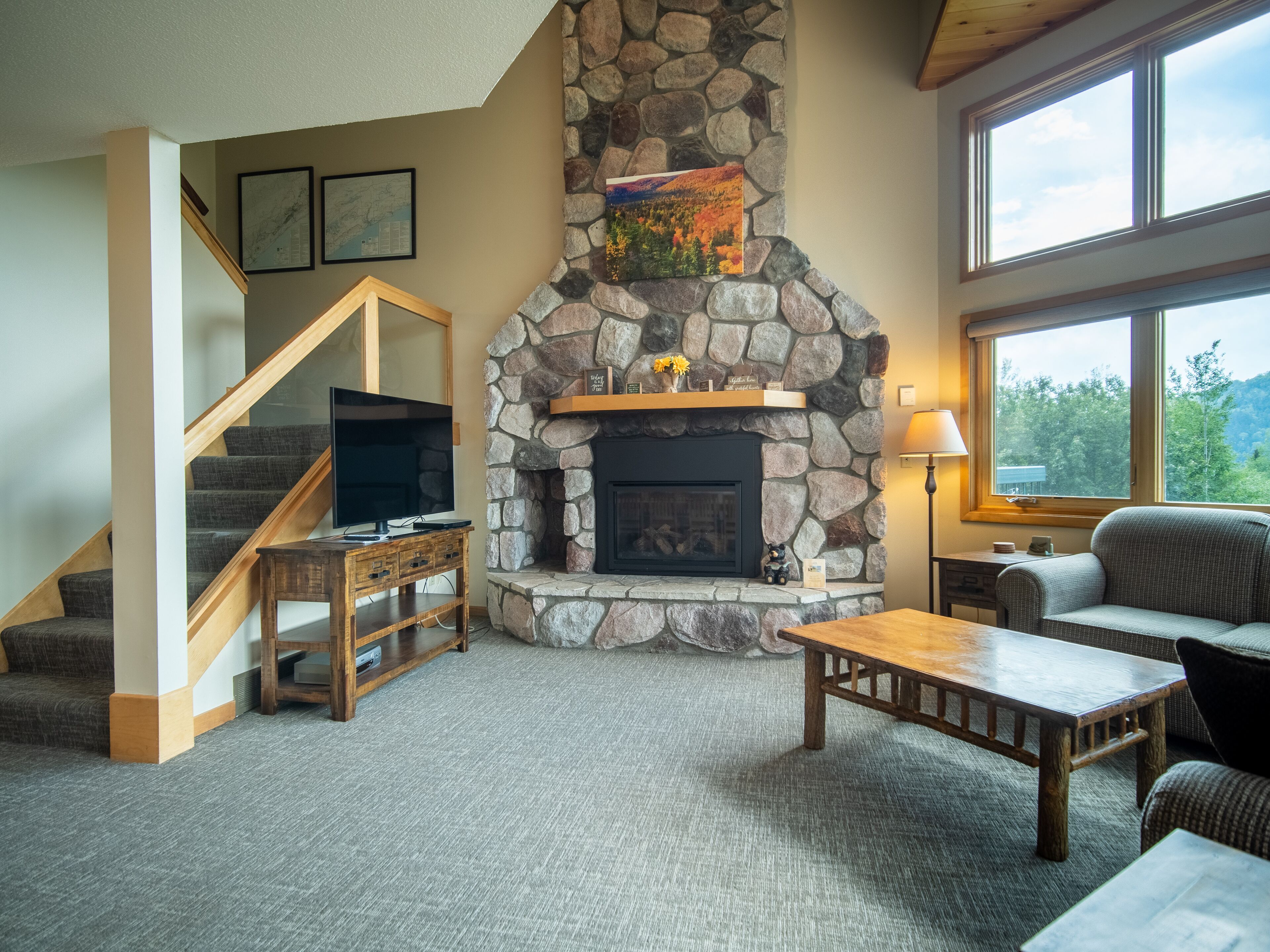 A living room with a stone fireplace, a television on a wooden stand, a sofa, and a staircase.
