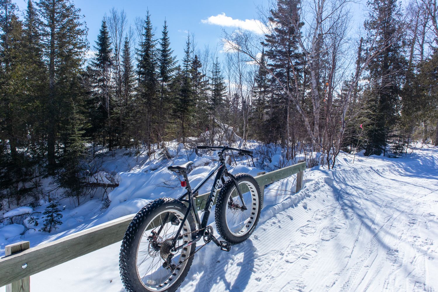 Een mountainbike geparkeerd op een houten leuning met uitzicht op een besneeuwd bospad.