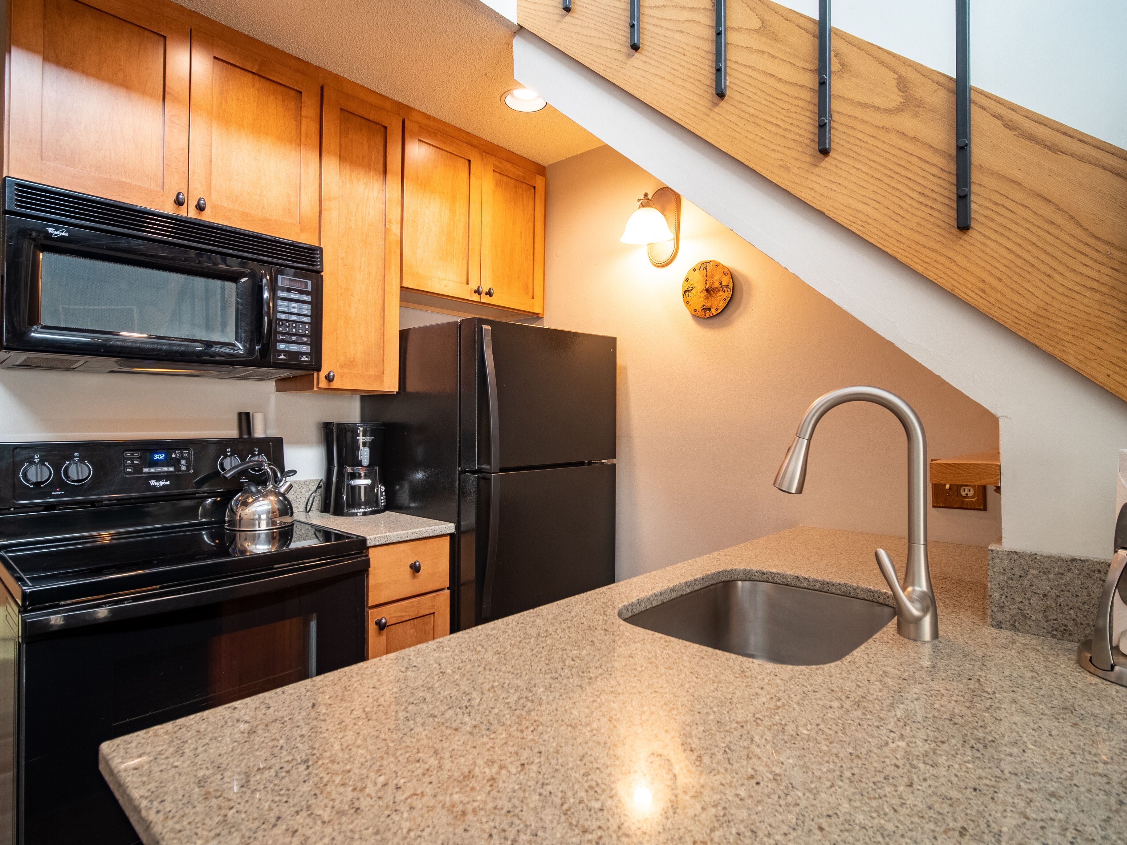 A kitchen with wooden cabinets, a stainless steel sink, a black refrigerator, a microwave, and a coffee maker.