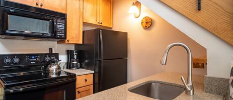 A kitchen with wooden cabinets, a stainless steel sink, a black refrigerator, a microwave, and a coffee maker.