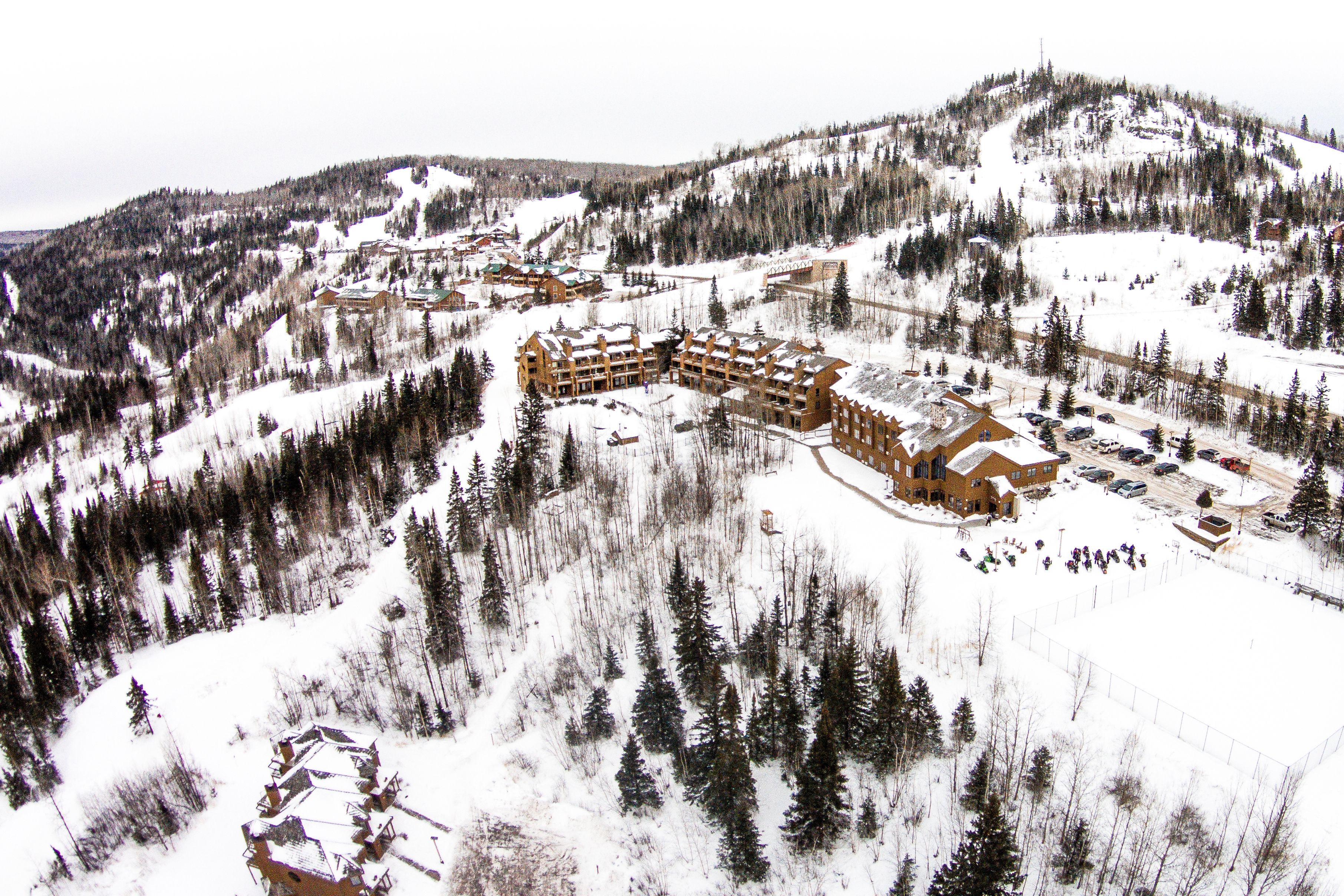 A large lodge with multiple buildings surrounded by snow-covered forest and hills.