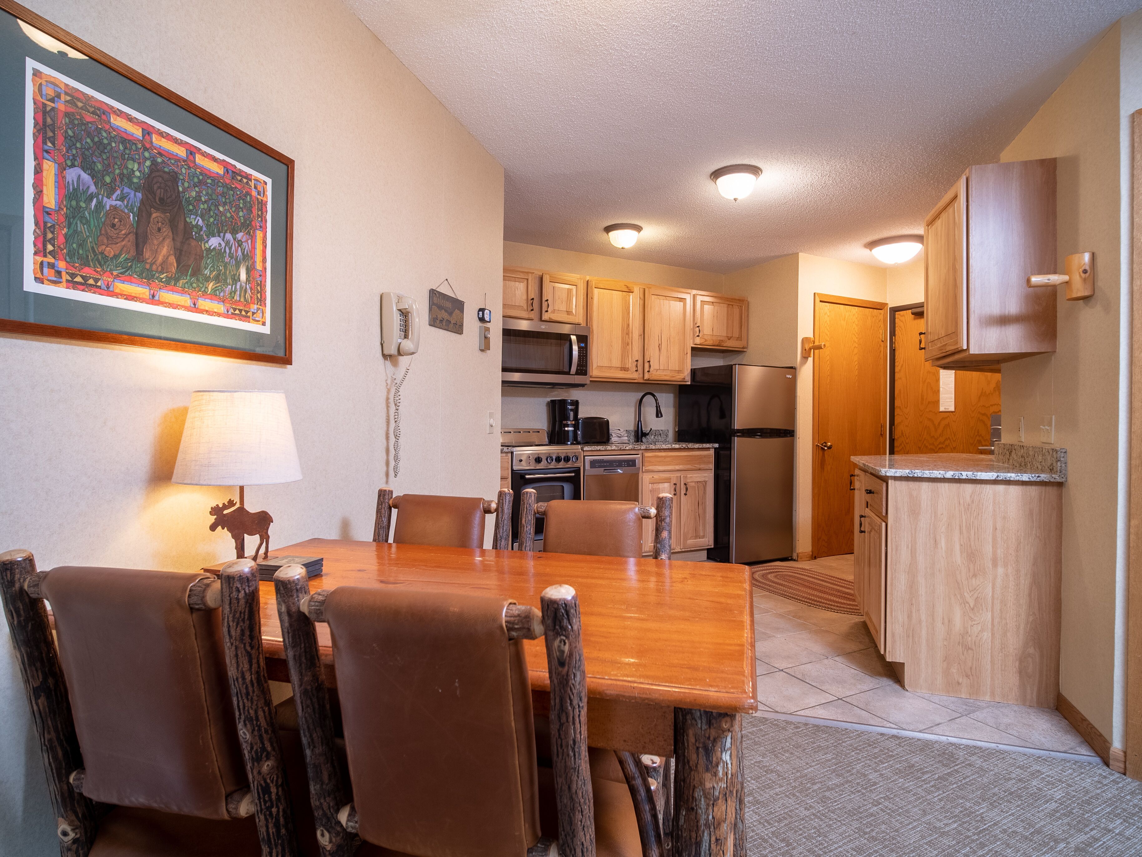 A compact kitchen with wooden cabinets, a refrigerator, stove, microwave, and a dining area with a wooden table and chairs.