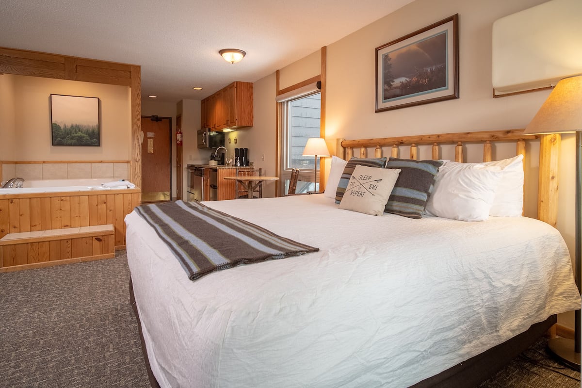 Une chambre avec un grand lit, une tête de lit en bois, une lampe de chevet et une vue sur la cuisine et la salle de bain.