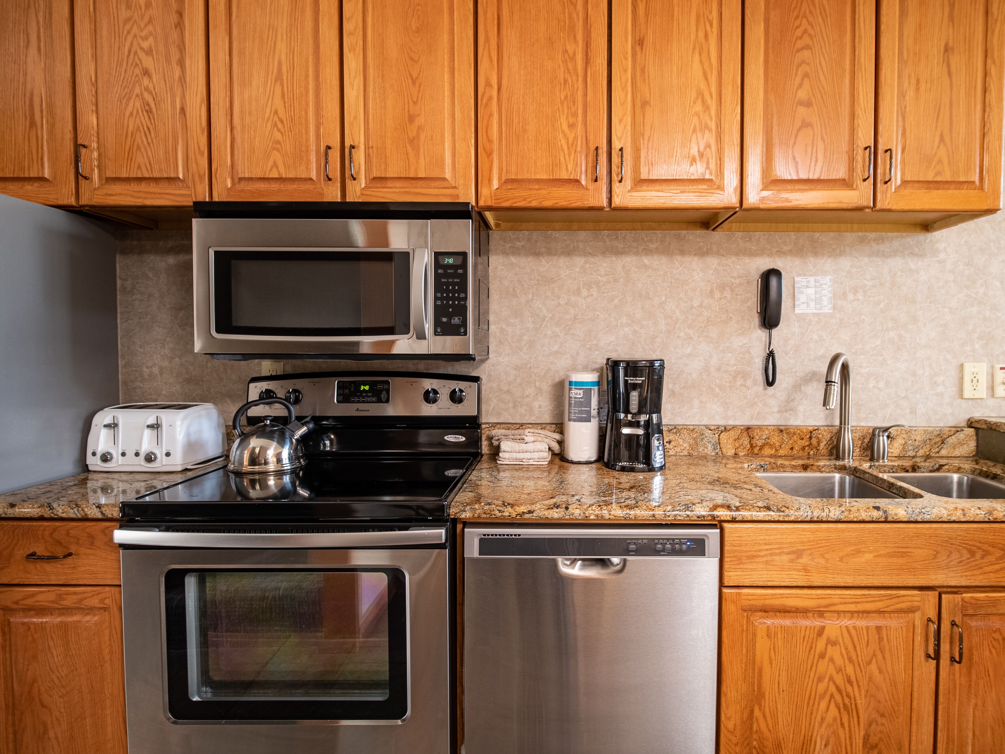 A kitchen with wooden cabinets, a microwave, a stove, a toaster, a coffee maker, and a dishwasher.