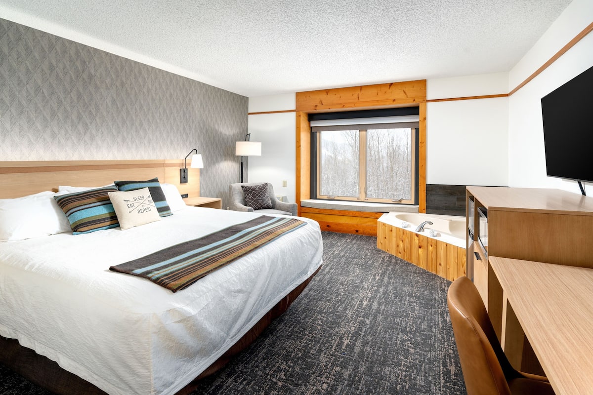 Une chambre d’hôtel avec un grand lit, un bureau, une chaise, une fenêtre, une baignoire et un téléviseur.