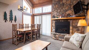 Una sala de estar acogedora con chimenea de piedra, un comedor con sillas de madera y un amplio ventanal que proporciona luz natural.