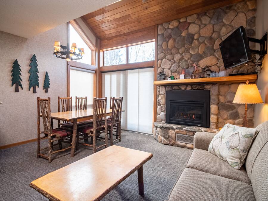 Una sala de estar acogedora con chimenea de piedra, un comedor con sillas de madera y un amplio ventanal que proporciona luz natural.