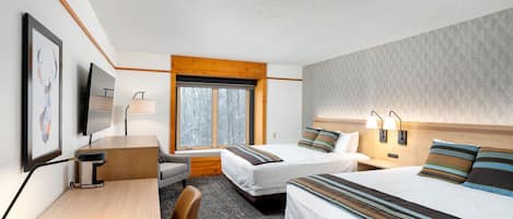 A hotel room with two beds, a desk, a chair, a TV, and a window with a view of trees.