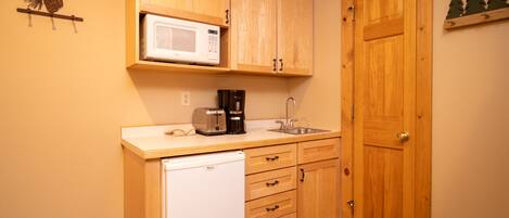 Cocina compacta con armarios de madera, microondas, tostadora, cafetera y lavavajillas.
