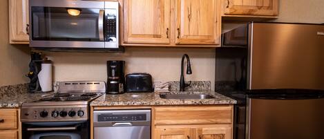 A kitchen with wooden cabinets, a stainless steel microwave, a toaster, a coffee maker, a dishwasher, a stove, and a refrigerator.