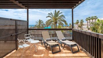Un espace extérieur abrité, doté de chaises longues et d’une table, offrant une vue sur une piscine et des palmiers.