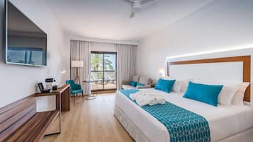 Habitación de hotel con cama, escritorio, silla, sofá, balcón con vistas y ventilador de techo.