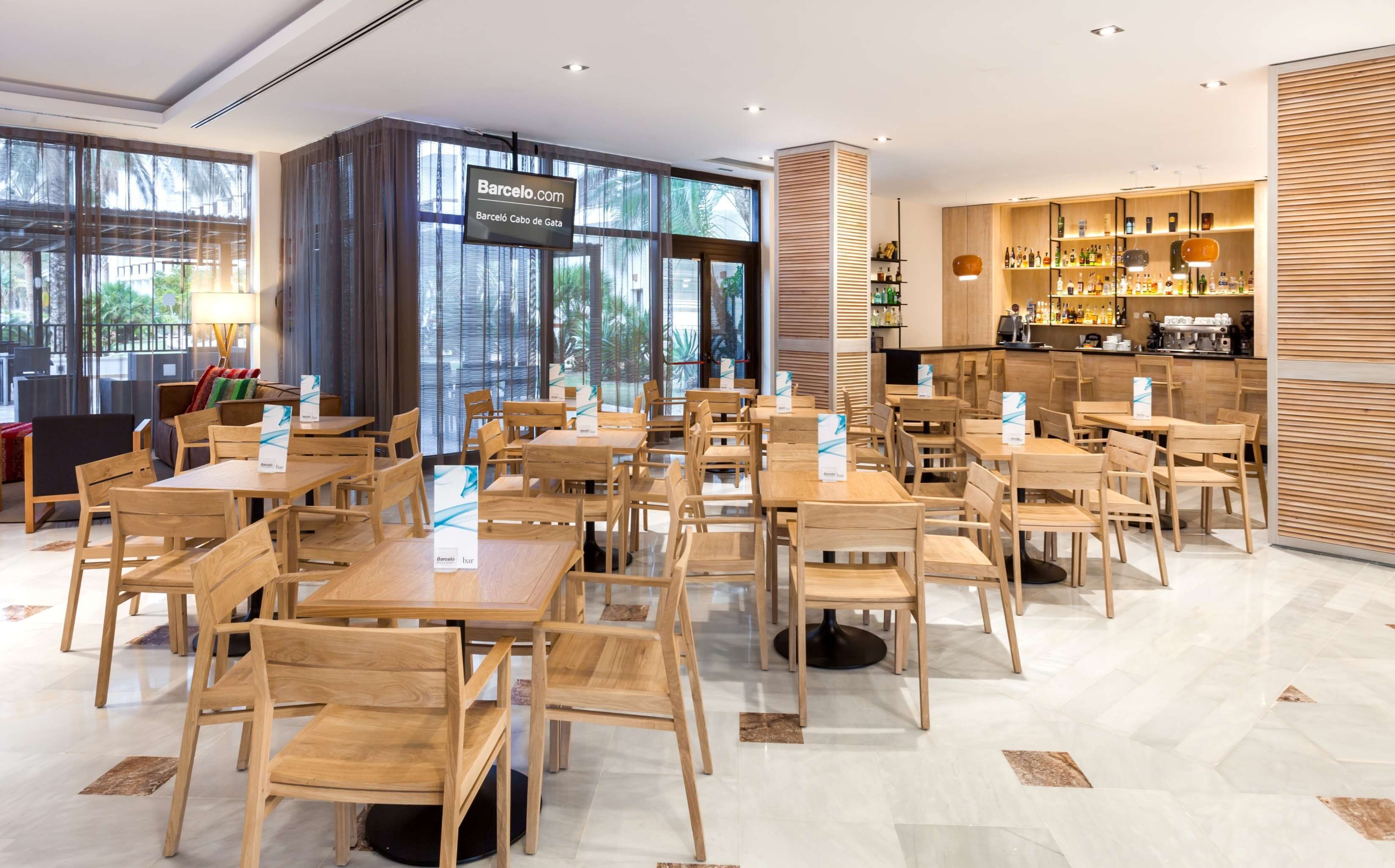 Een modern restaurant met houten tafels en stoelen, een bar met flessenrekken, en grote ramen met uitzicht op het omliggende landschap.