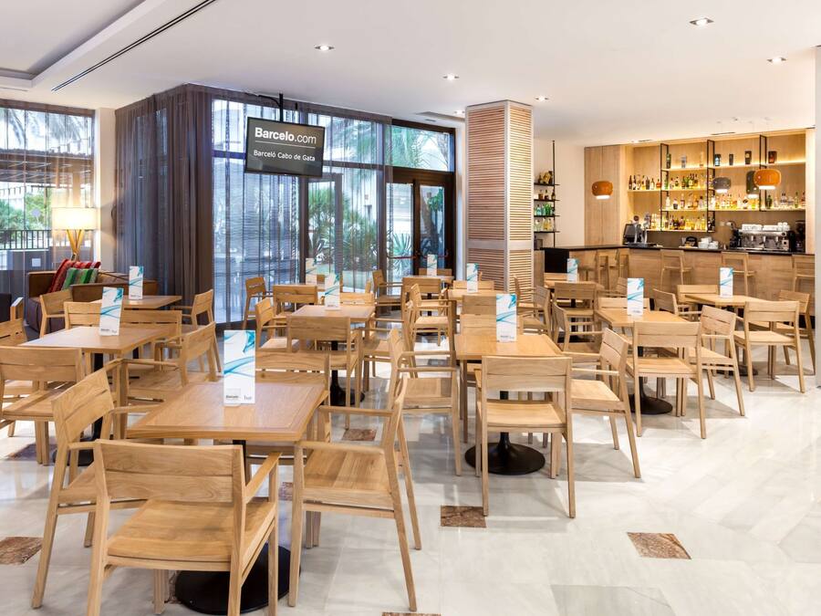 Ein modernes Restaurant mit Holztischen und -stühlen, einer Bar mit Flaschenregalen und großen Fenstern mit Blick ins Freie.