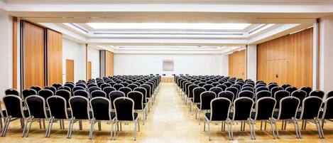 A conference room with rows of chairs, a wooden floor, and a high ceiling with skylights.