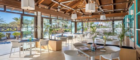 Un espacio de comedor al aire libre con vigas de madera, sillas blancas y lámparas colgantes.